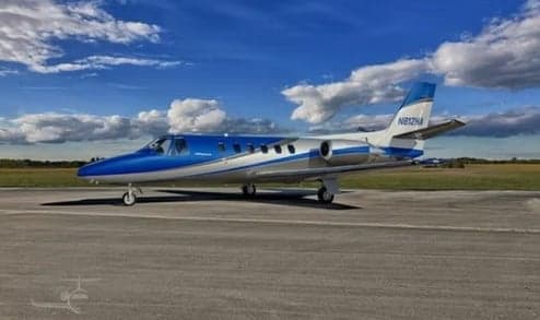 A blue and silver business jet, tail number N812HA, parked on an airfield under a partly cloudy sky.