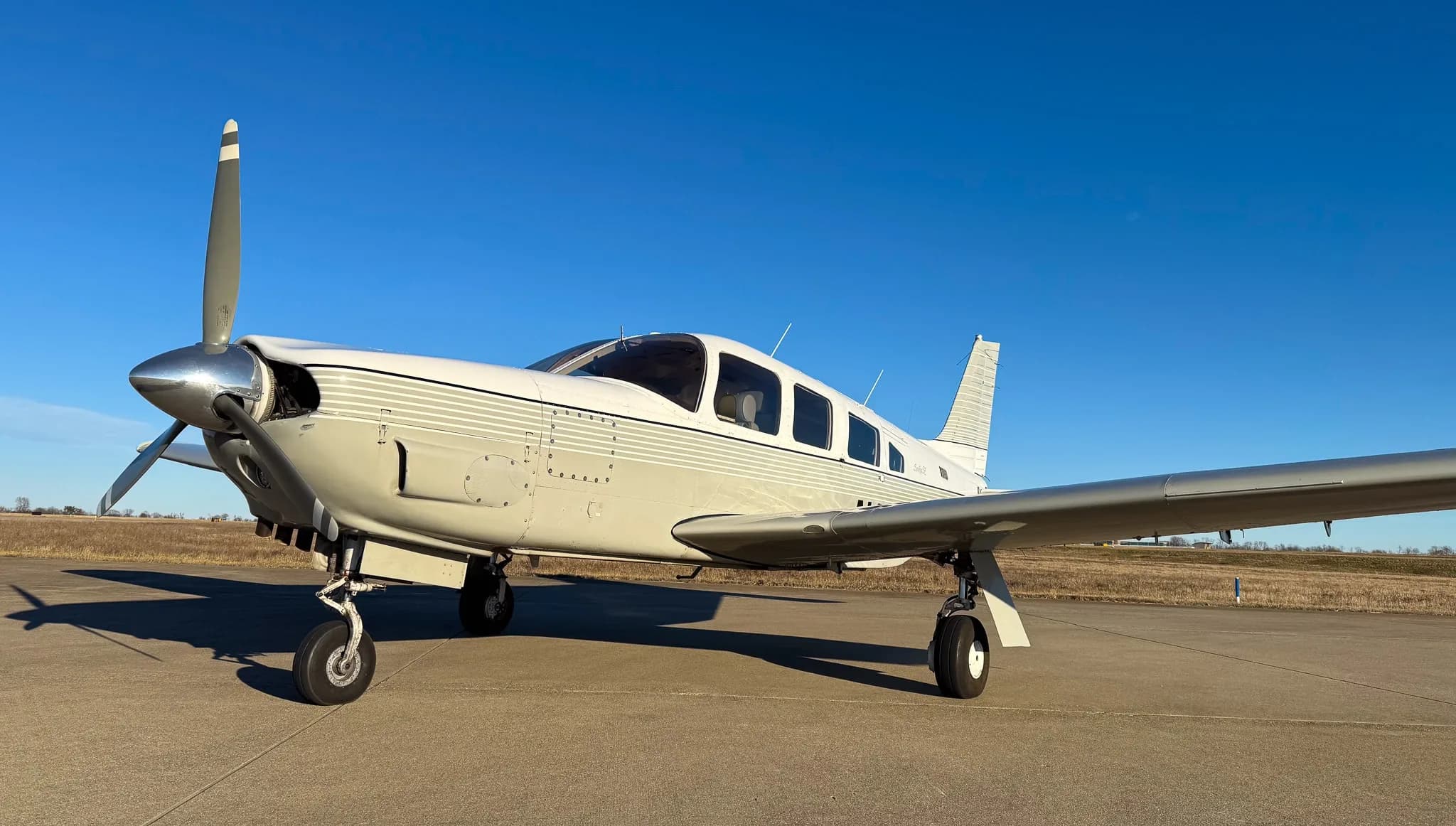 A front three-quarter view of a white Piper Saratoga SP (N1622P) with grey stripes on an airfield.