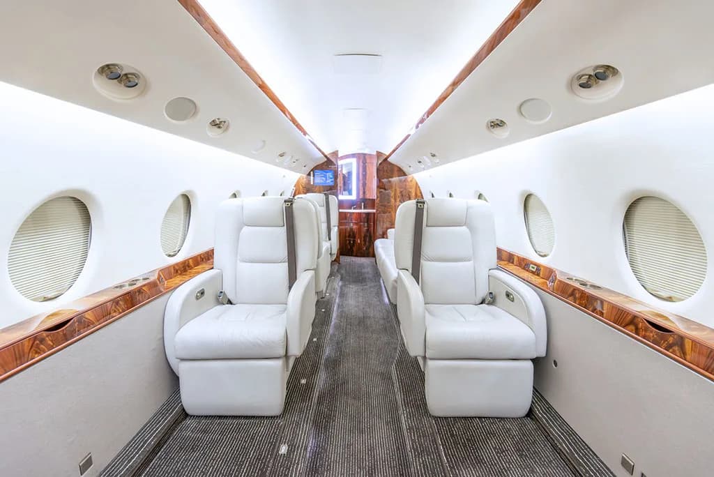 The luxurious interior cabin of a private jet with white leather seats and wood paneling.
