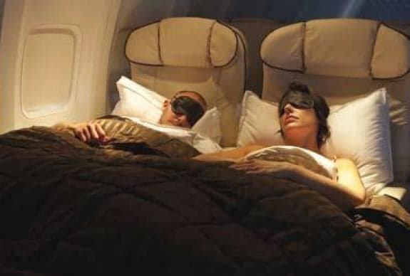 Interior of a private jet with a bed and sleeping passengers.