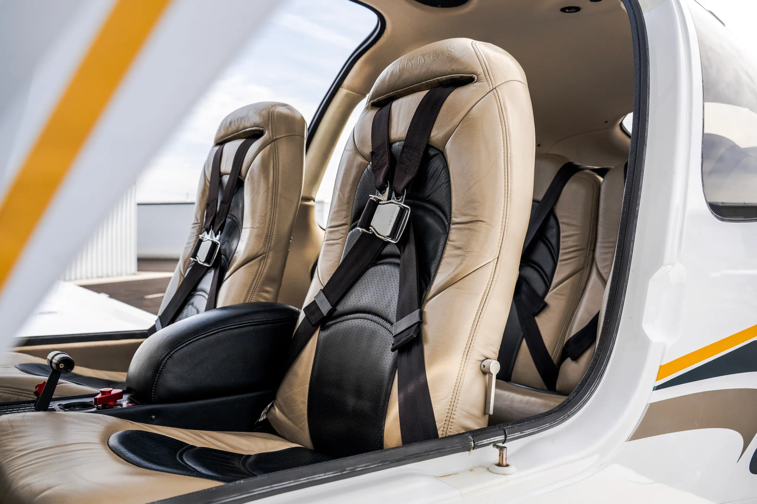 The interior cabin of an aircraft, showing two tan and black leather seats with seatbelts.