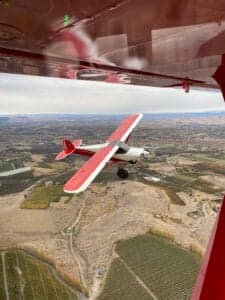 A red and white Cubcrafters FX-3 aircraft in flight over a rural landscape.
