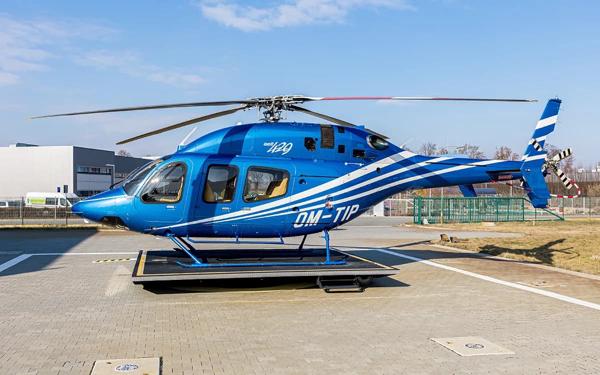 A blue Bell 429 helicopter with white and light blue stripes is parked on a helipad under a clear sky.