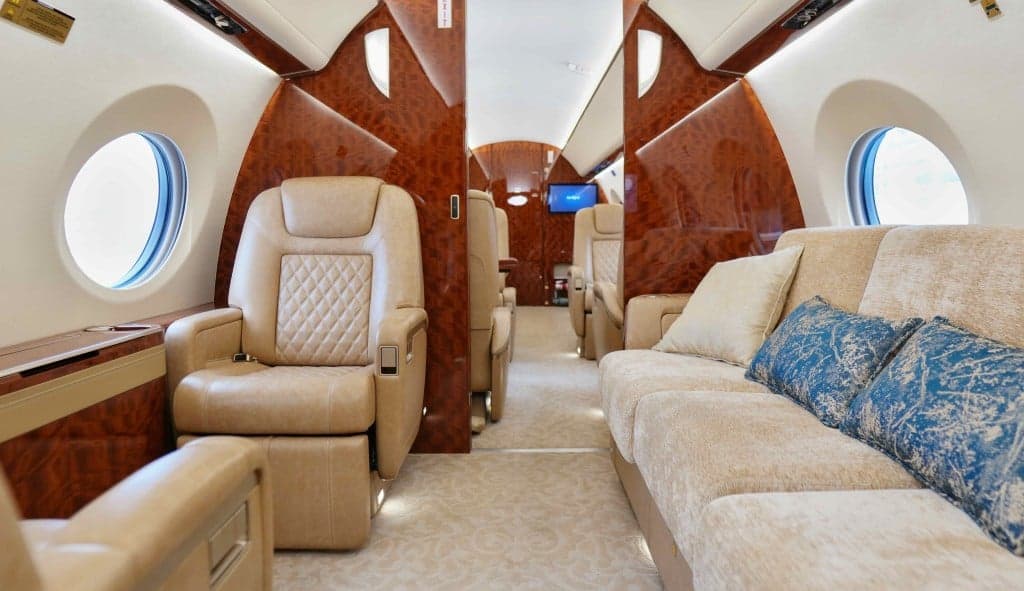 The interior of the aircraft features tan leather seats, wood trim, and a large screen.