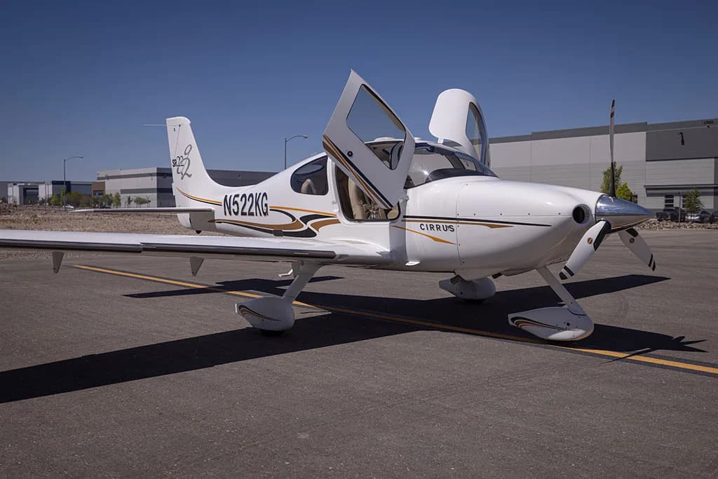 A white Cirrus SR22 aircraft with gold and black stripes, registration N522KG, parked on an airfield with both doors open.