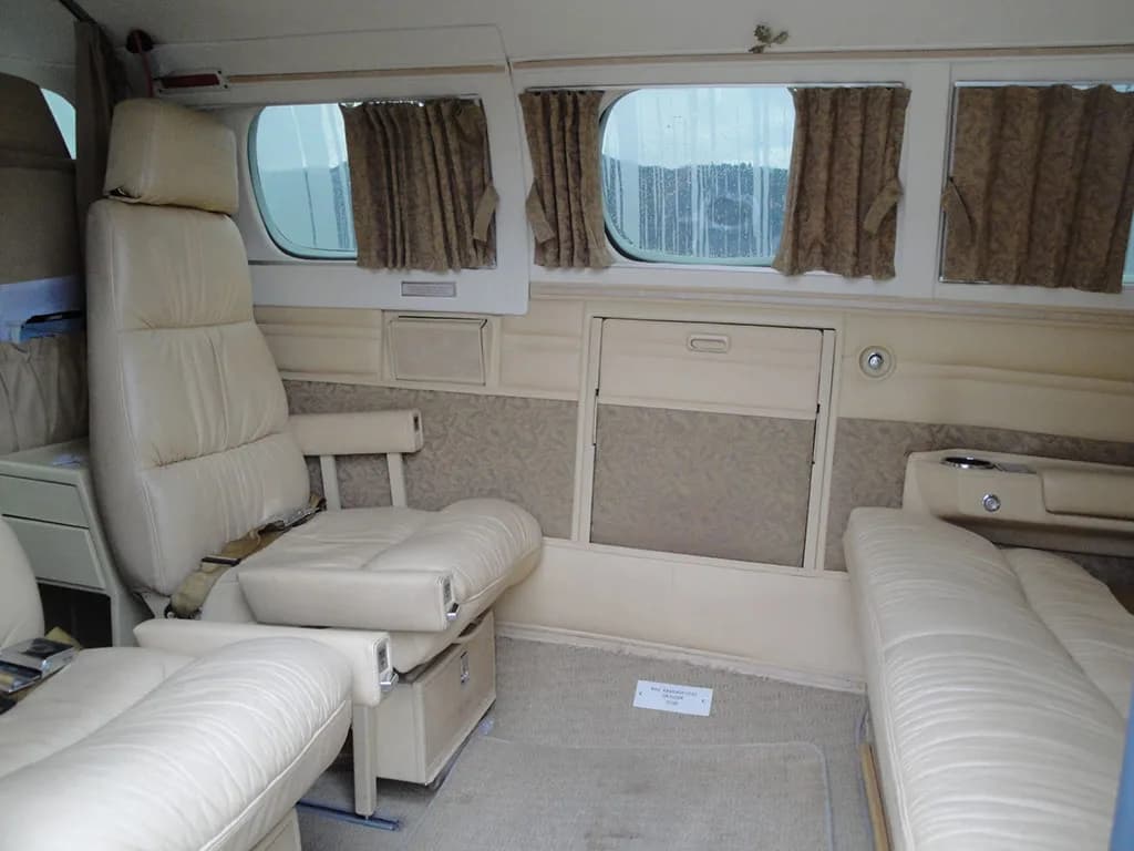 The aircraft's beige interior cabin features cream leather seats, patterned wall panels, and windows with brown curtains.