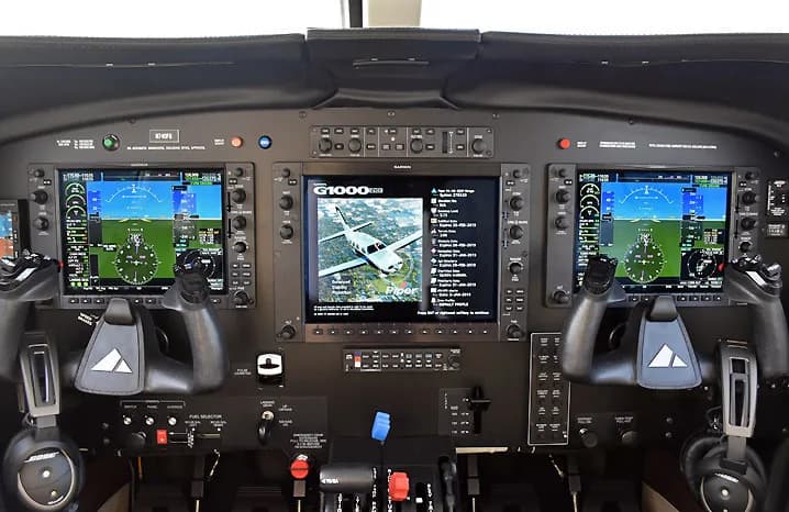 The cockpit instrument panel of an aircraft, featuring multiple Garmin G1000 displays and control yokes.