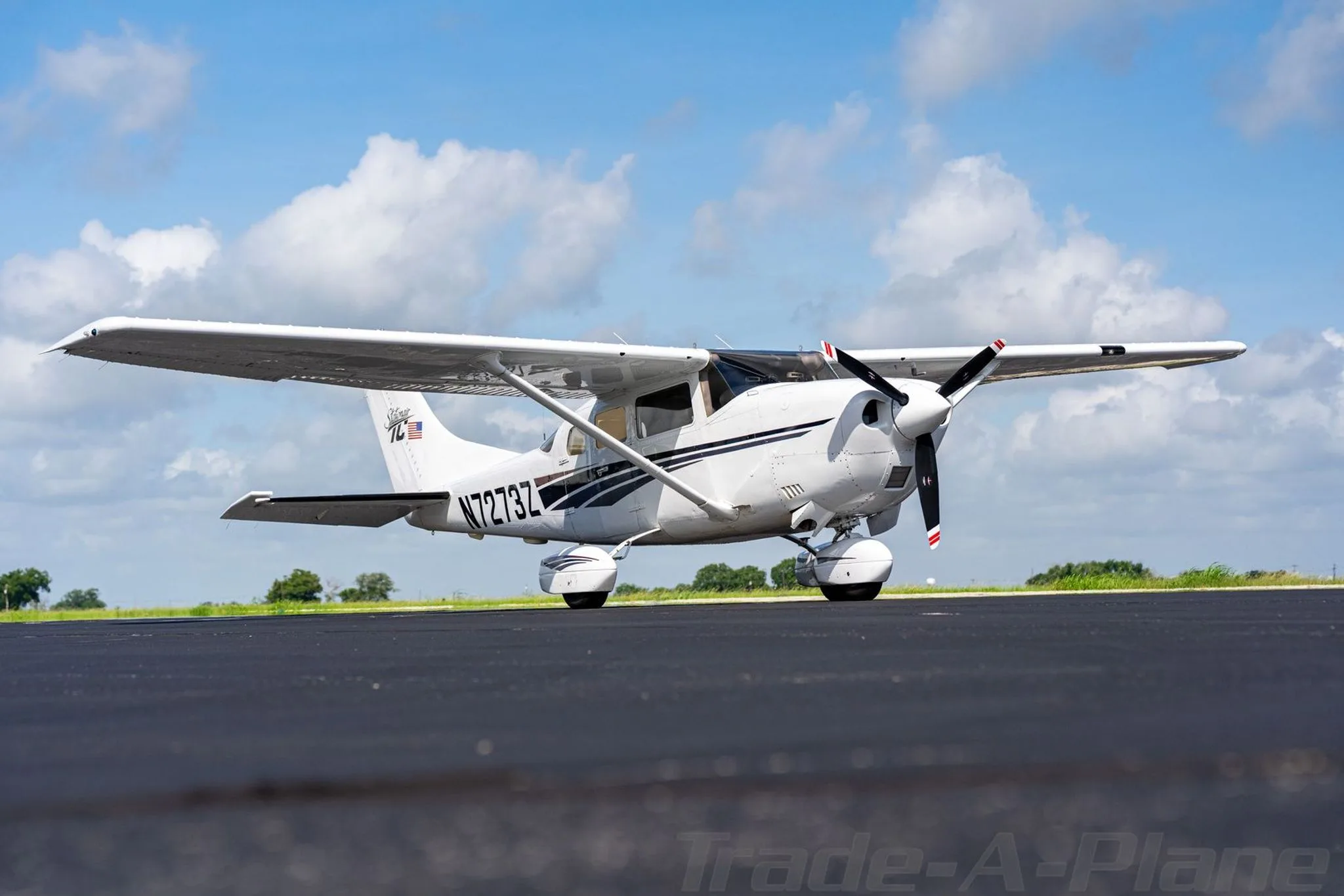 A white Cessna Stationair TC with dark blue and gray stripes on a tarmac under a partly cloudy sky.