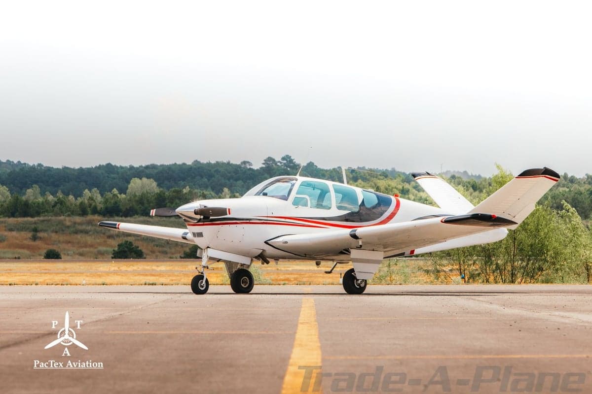 Side profile of a white single-engine aircraft with red and black stripes parked on an airfield.