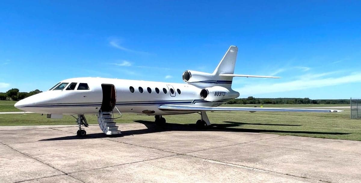 A white Dassault Falcon 900 with blue stripes is parked on the tarmac.