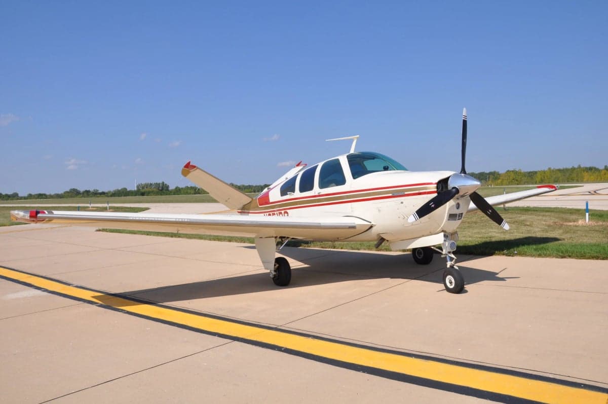 A Beechcraft Bonanza aircraft is parked on the tarmac on a sunny day.