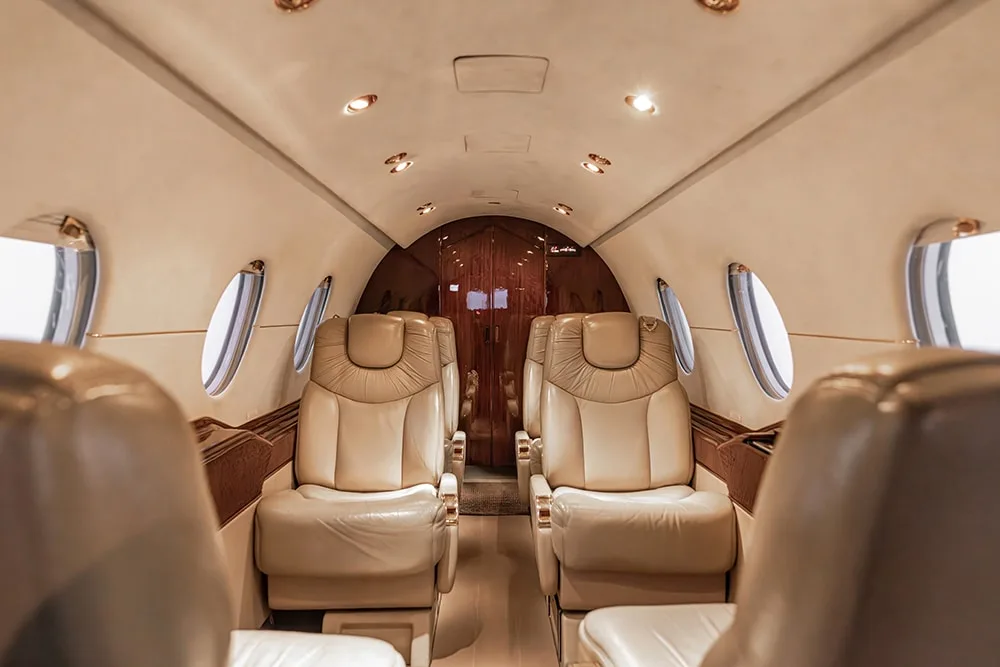 View down the aisle of a private jet cabin with light-colored leather seats and dark wood accents.