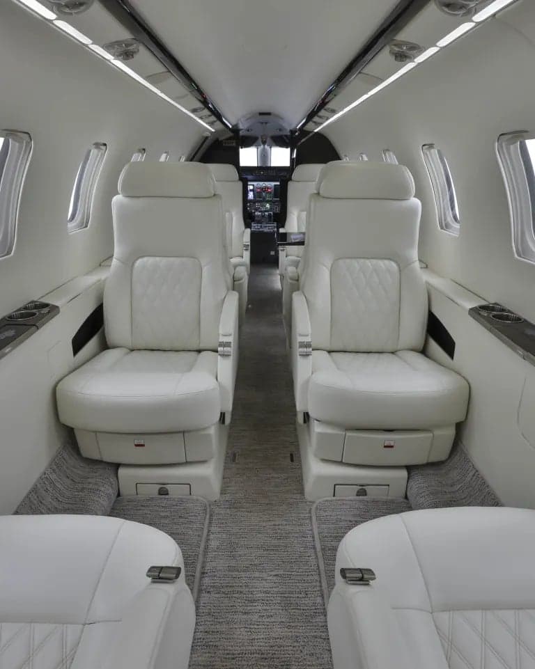 Full view of the aircraft interior with white leather seats and a view of the cockpit.