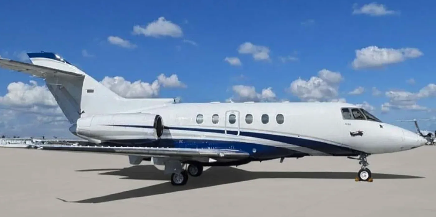 A white business jet with blue and grey stripes on the tarmac under a blue sky.