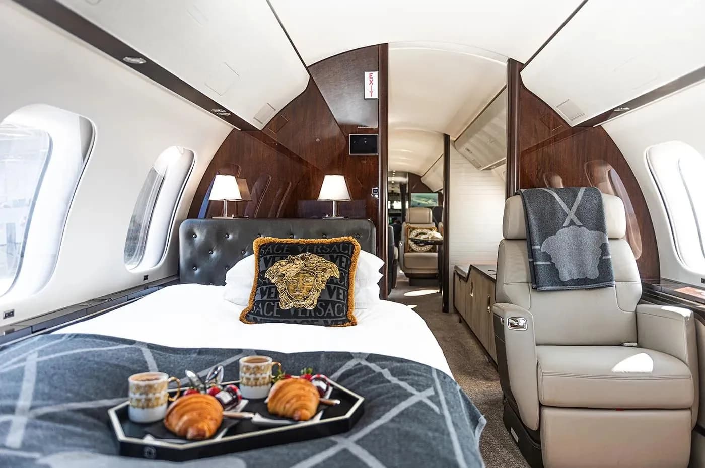 A private jet cabin configured with a bed, a side chair, and a tray with croissants and coffee.