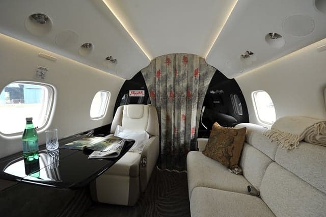 A private jet's interior cabin with a set table, a single seat, a sofa, and a patterned curtain separating sections.