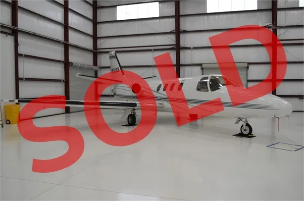A white light jet with dark stripes, registration N671BB, parked inside a hangar.