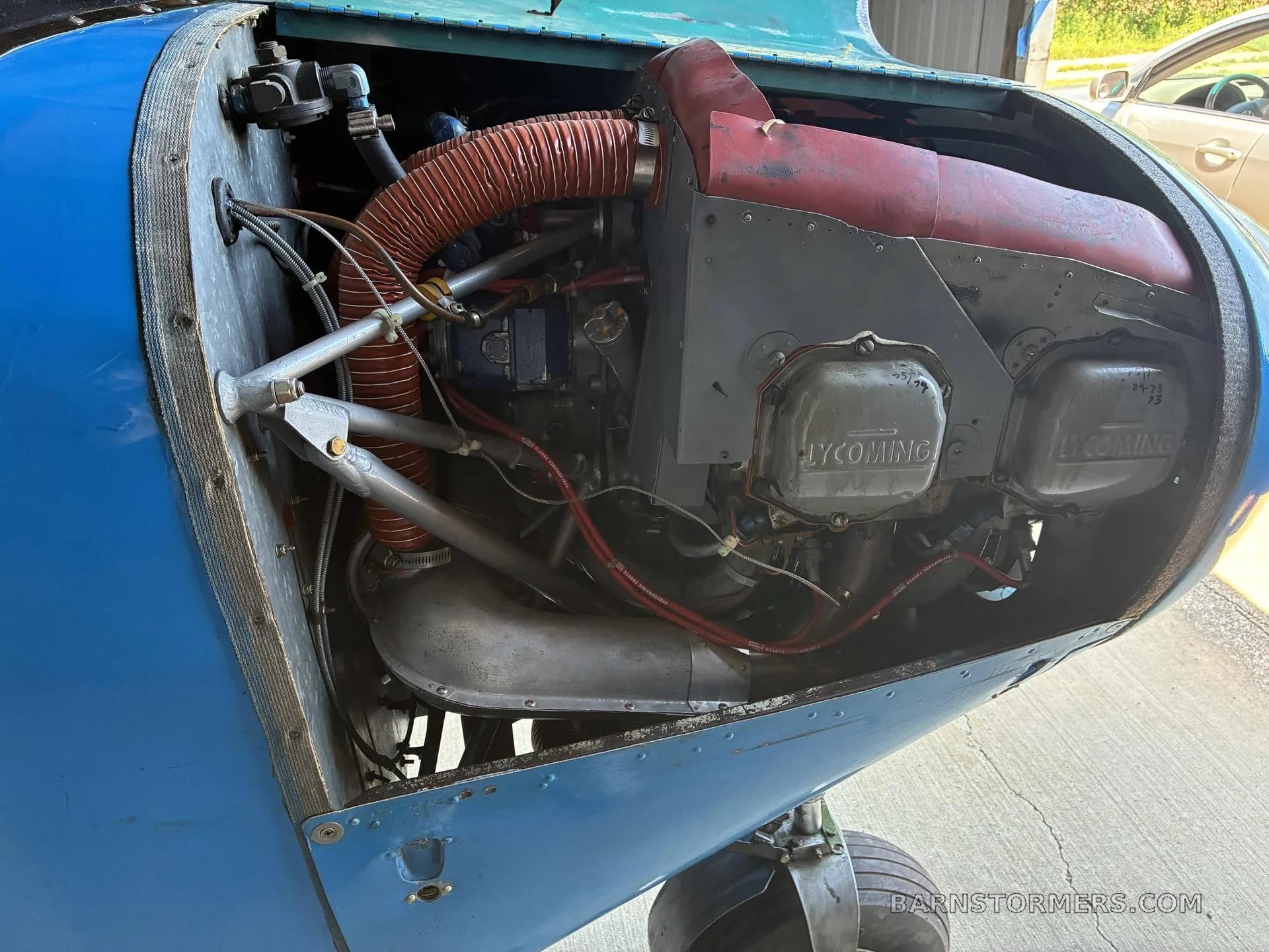 The open engine compartment of a blue aircraft, revealing a Lycoming engine with red and silver components.