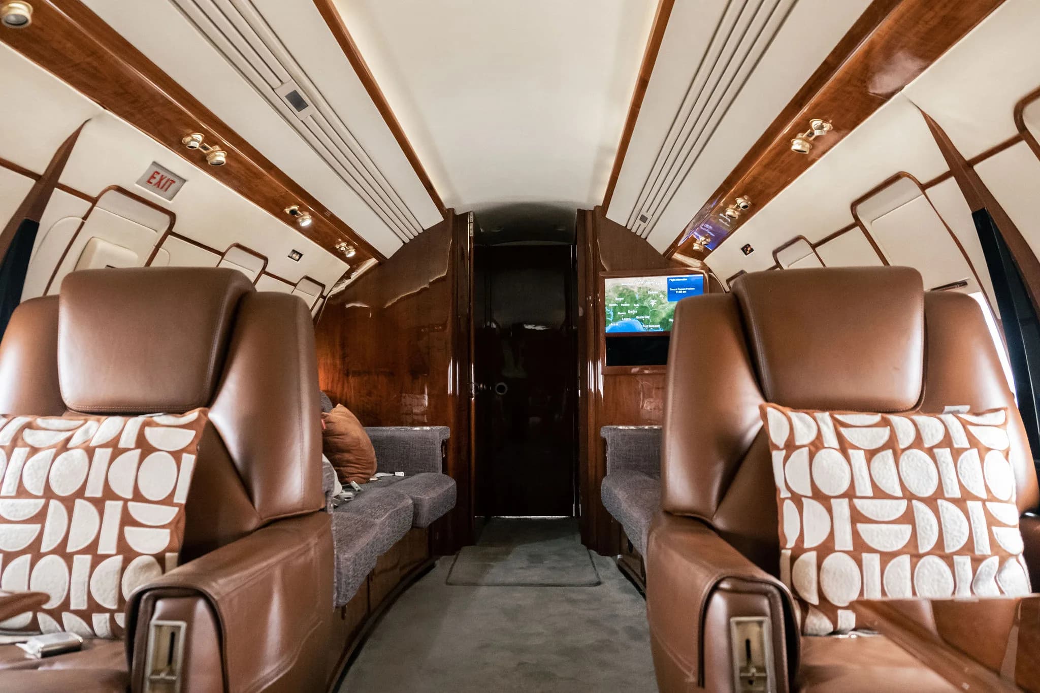 Symmetrical view of a private jet cabin aisle with brown leather seats and a sofa on each side.