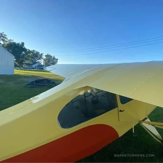 An overhead view of the yellow and orange aircraft's wing and fuselage, parked on a grassy field.