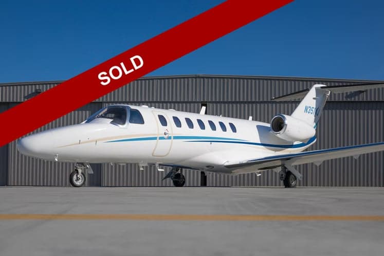 A white Cessna Citation CJ3 aircraft with blue and gold accents is parked in front of a hangar, with a red 'SOLD' banner across the image.