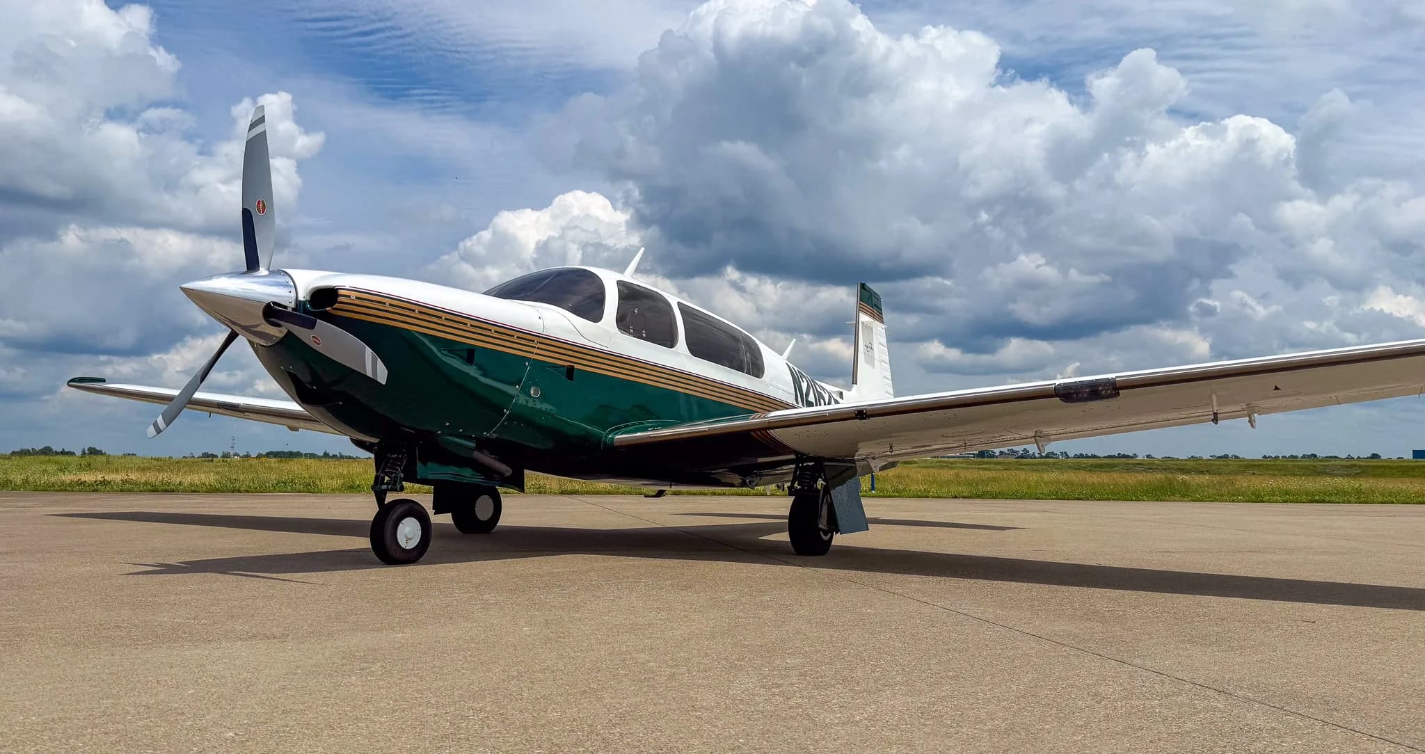 A white and green Mooney M20 aircraft with registration N21625 parked on an airfield under a cloudy sky.
