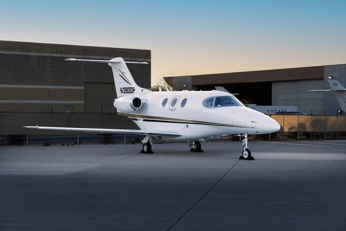 A white business jet with gold and black stripes, tail number N390DP, parked on an airport tarmac at sunset.