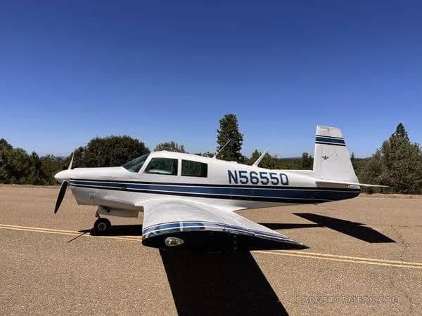 A white single-engine propeller aircraft with blue stripes (N5655Q) is parked on an asphalt surface, viewed from the side.