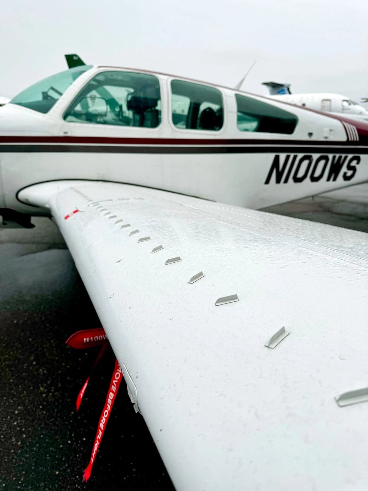 N100WS Bonanza aircraft parked on the tarmac with other aircraft and a building in the background.