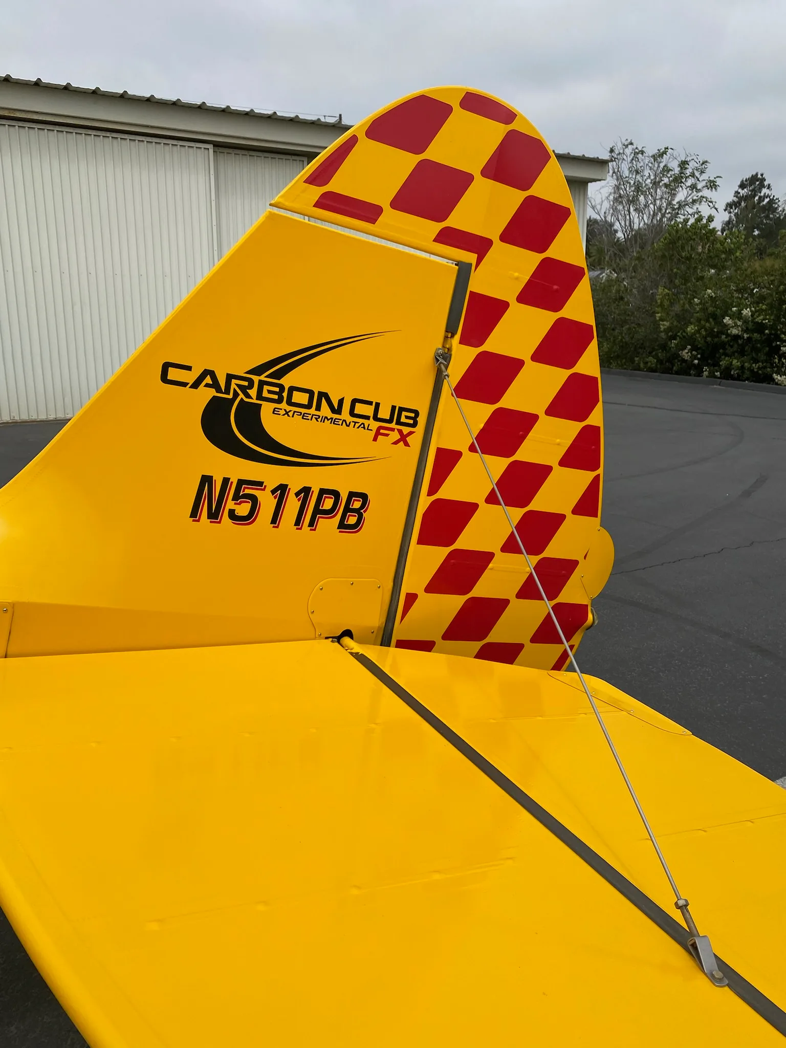 Tail of a yellow Carbon Cub aircraft with red checkered pattern and N number.