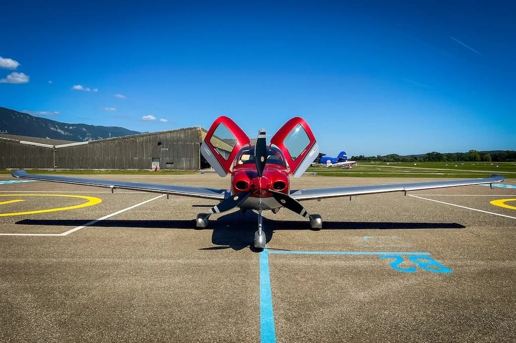 Front view of a red and silver Cirrus SR22 aircraft with both doors open, parked on an airfield.