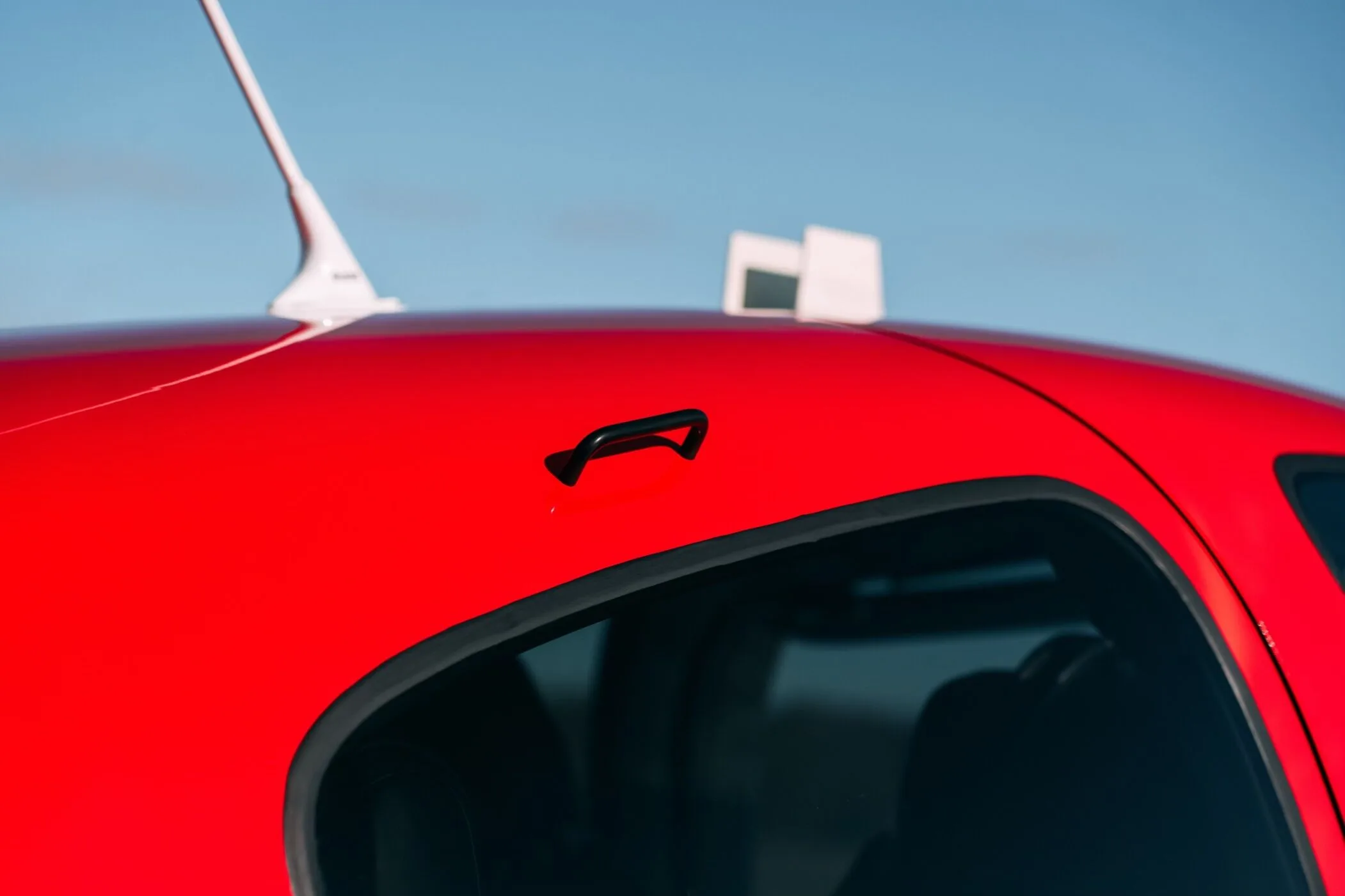 A close-up of the red top fuselage of the Cirrus SR22T aircraft, showing an antenna and handle.