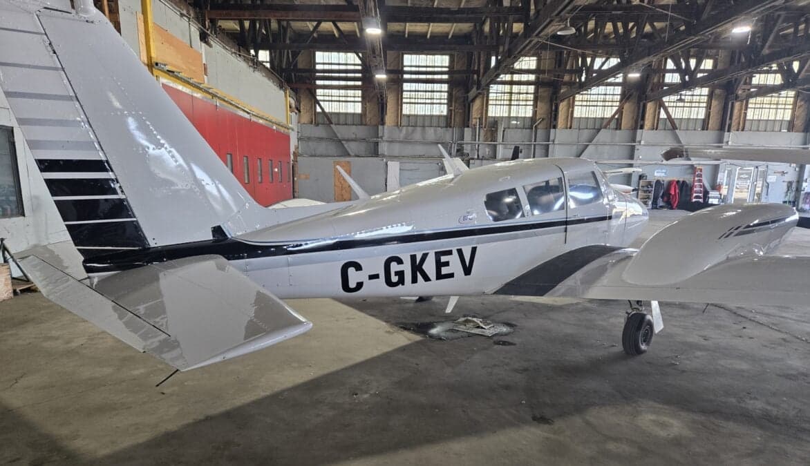 A white and black Piper PA-39 Twin Comanche is parked in a hangar.