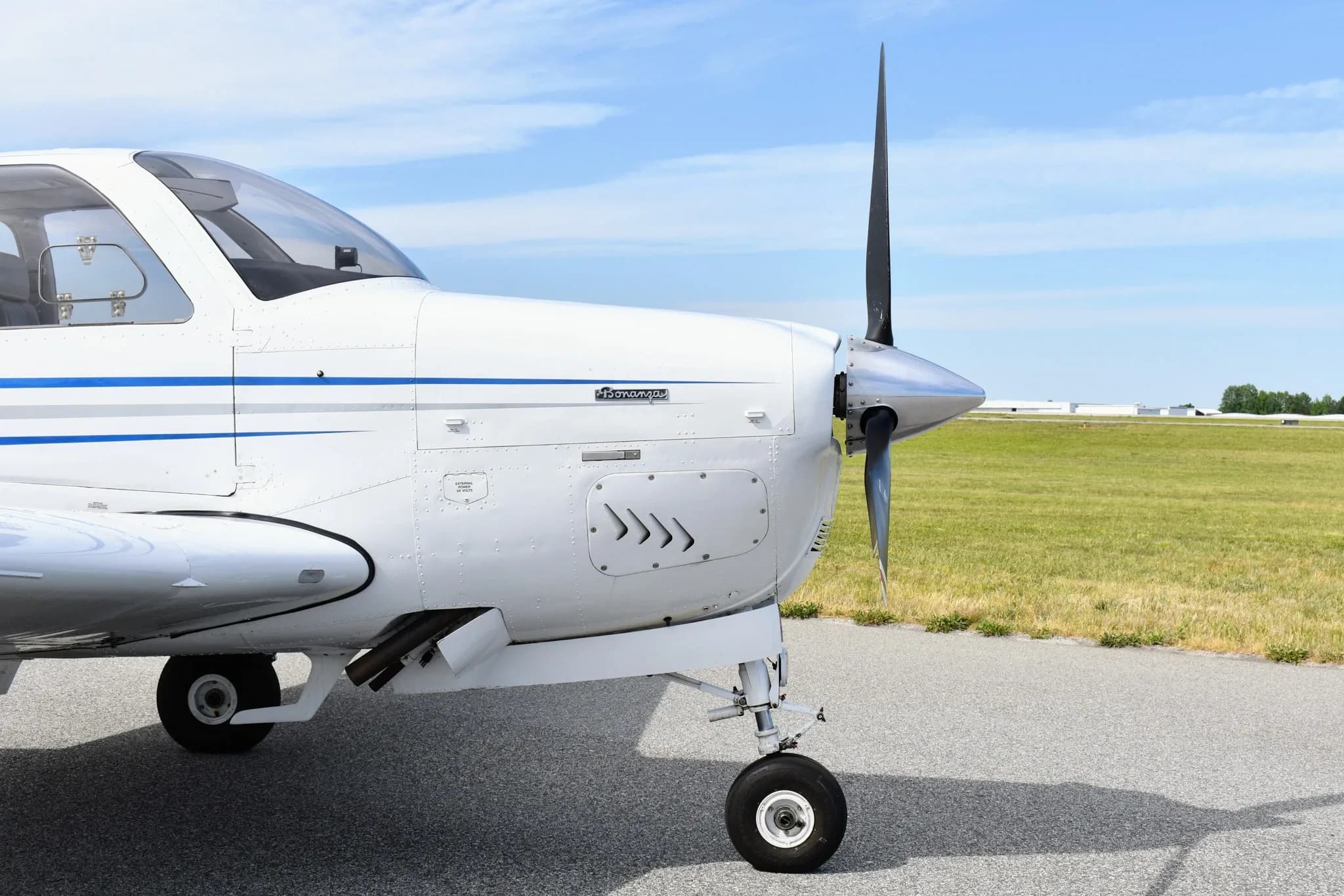 A close-up side view of the nose and propeller of a white Beechcraft Bonanza F33A.