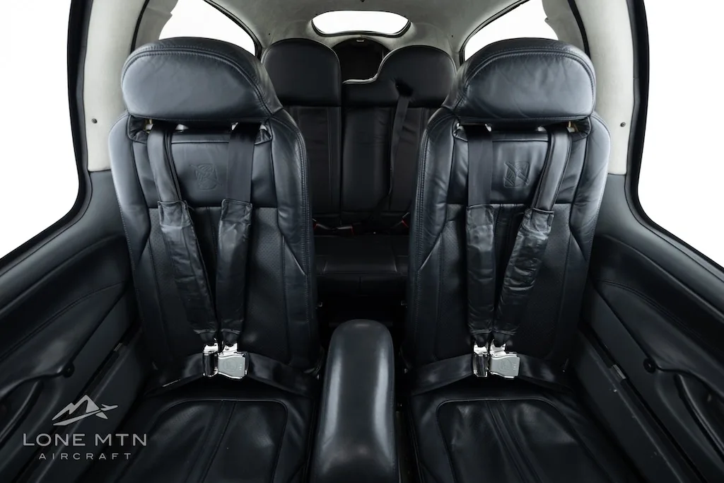 The black leather front and rear seats of a small aircraft cabin, viewed from the front, with seatbelts visible.