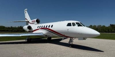 A white jet aircraft with red and black striping is parked on the tarmac.