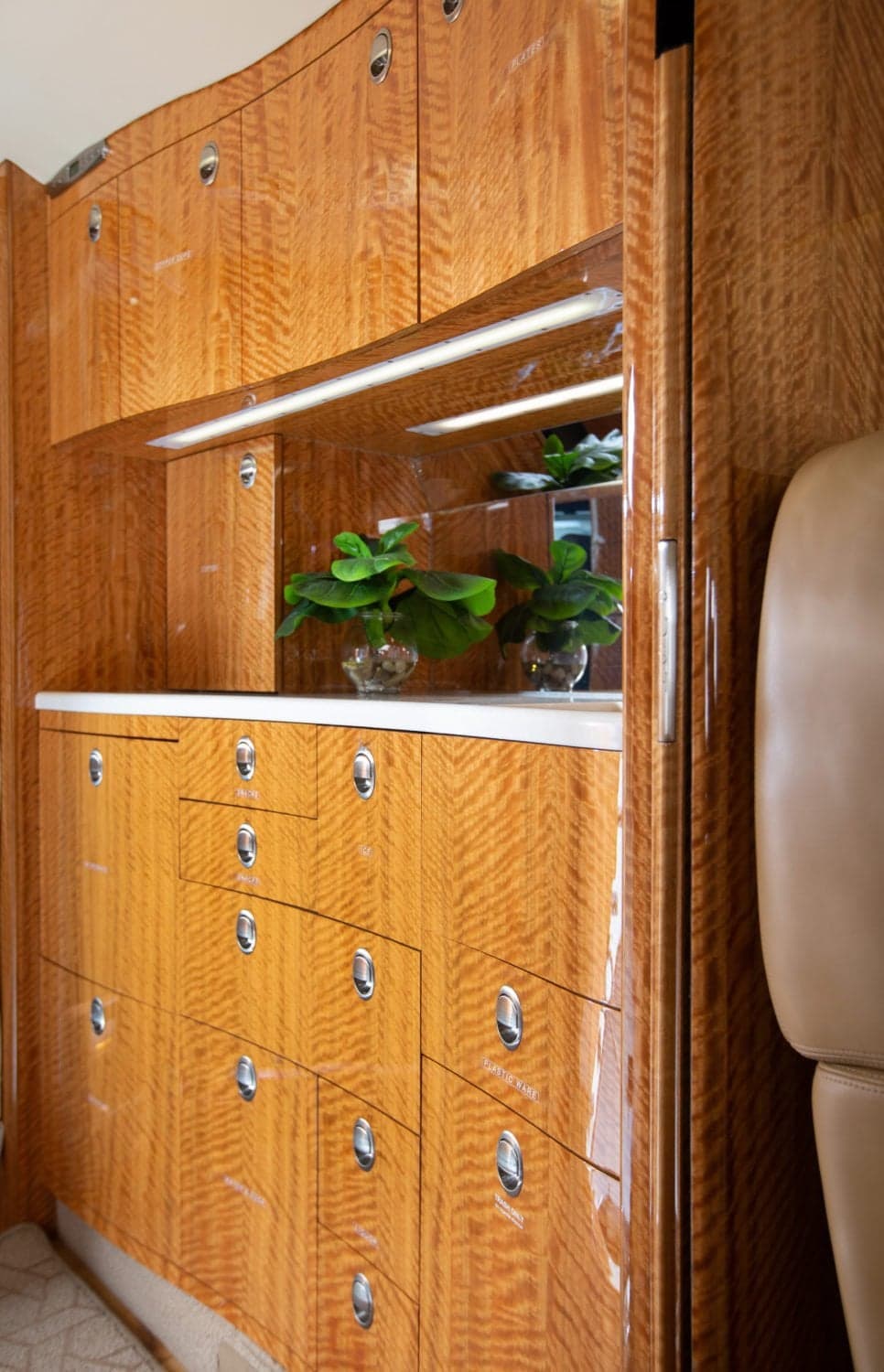Detailed view of aircraft cabinetry with polished wood, a small counter, and decorative plants reflected in a mirror.