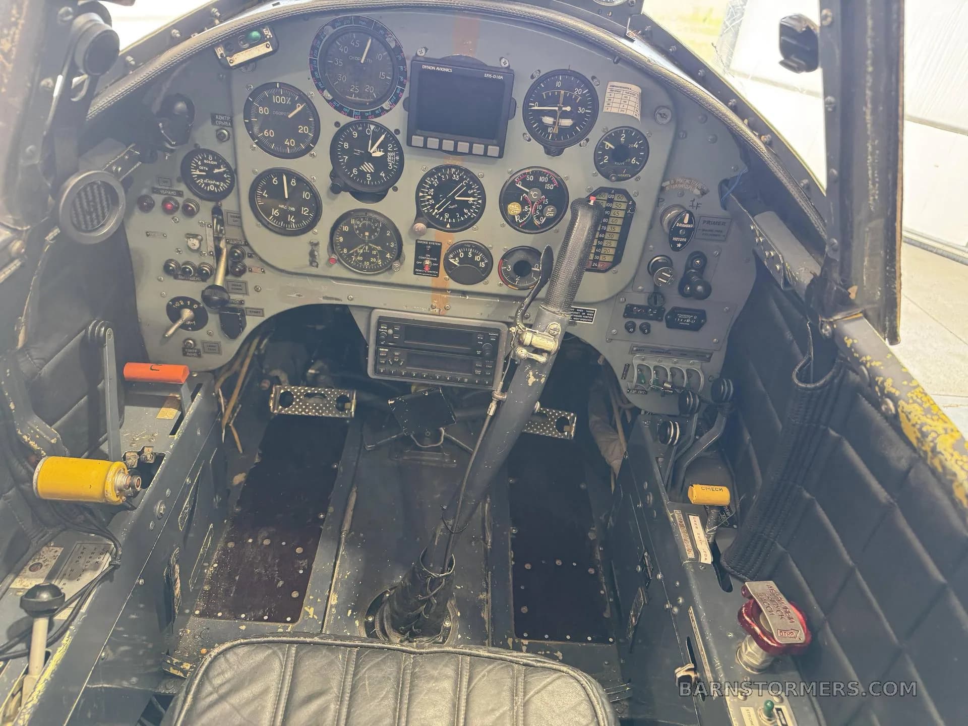 A detailed view of a vintage aircraft cockpit with numerous analog gauges, a control stick, and a black padded seat.