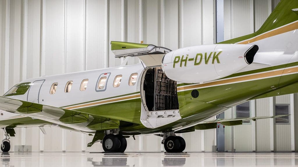 A white and green business jet, registration PH-DVK, with its cargo door open in a hangar.