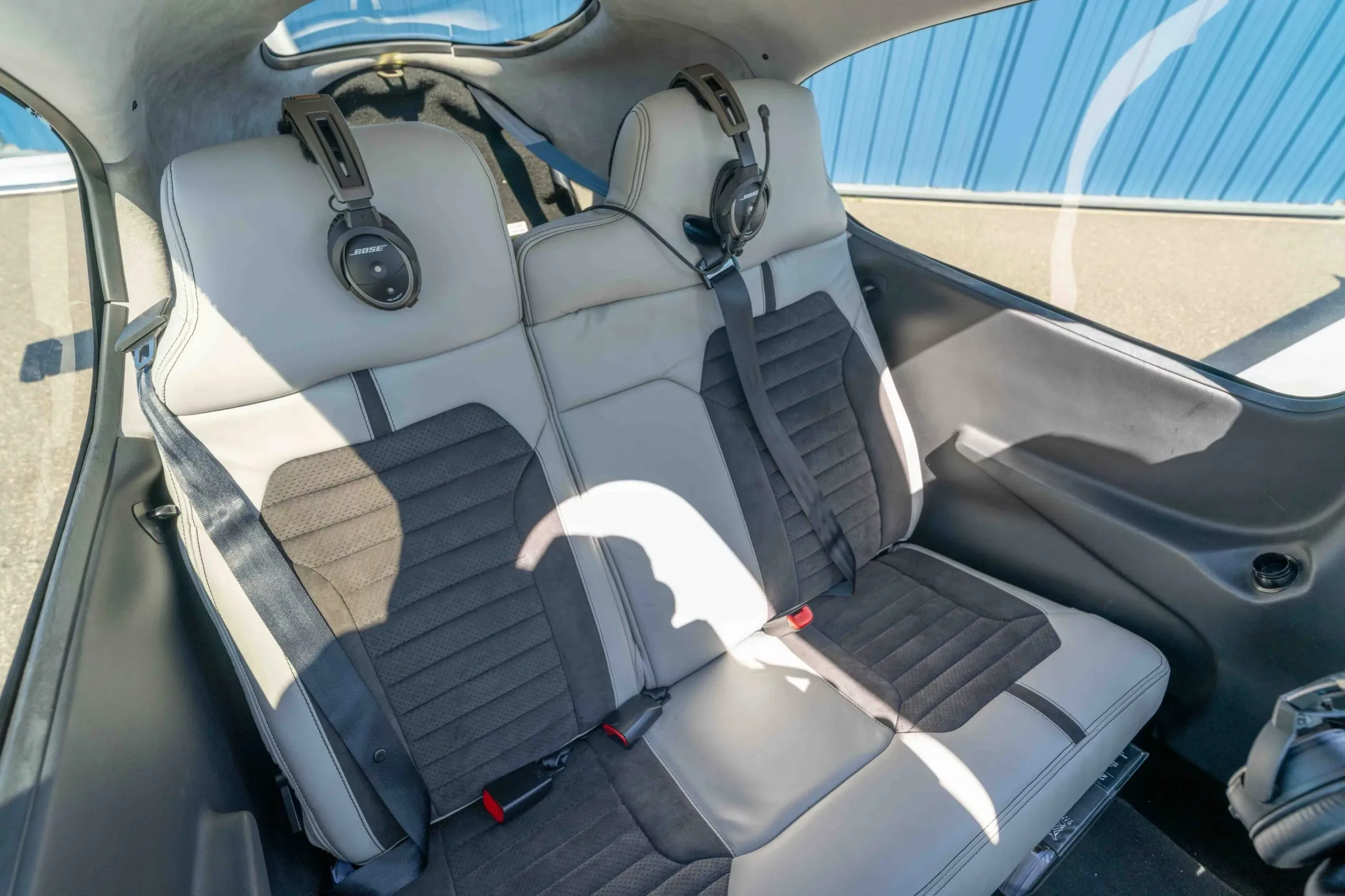 The light gray and dark gray two-tone rear passenger seats of the aircraft, with two headsets hanging on the headrests.