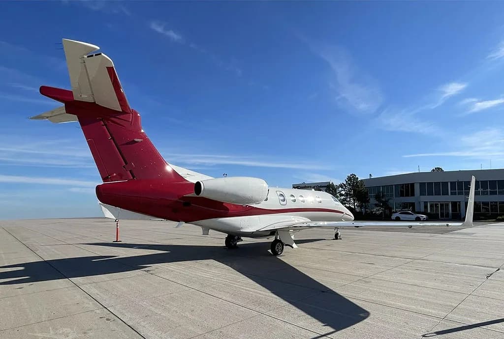 A rear view of a white and red Embraer Phenom 300 private jet parked on an airport tarmac.