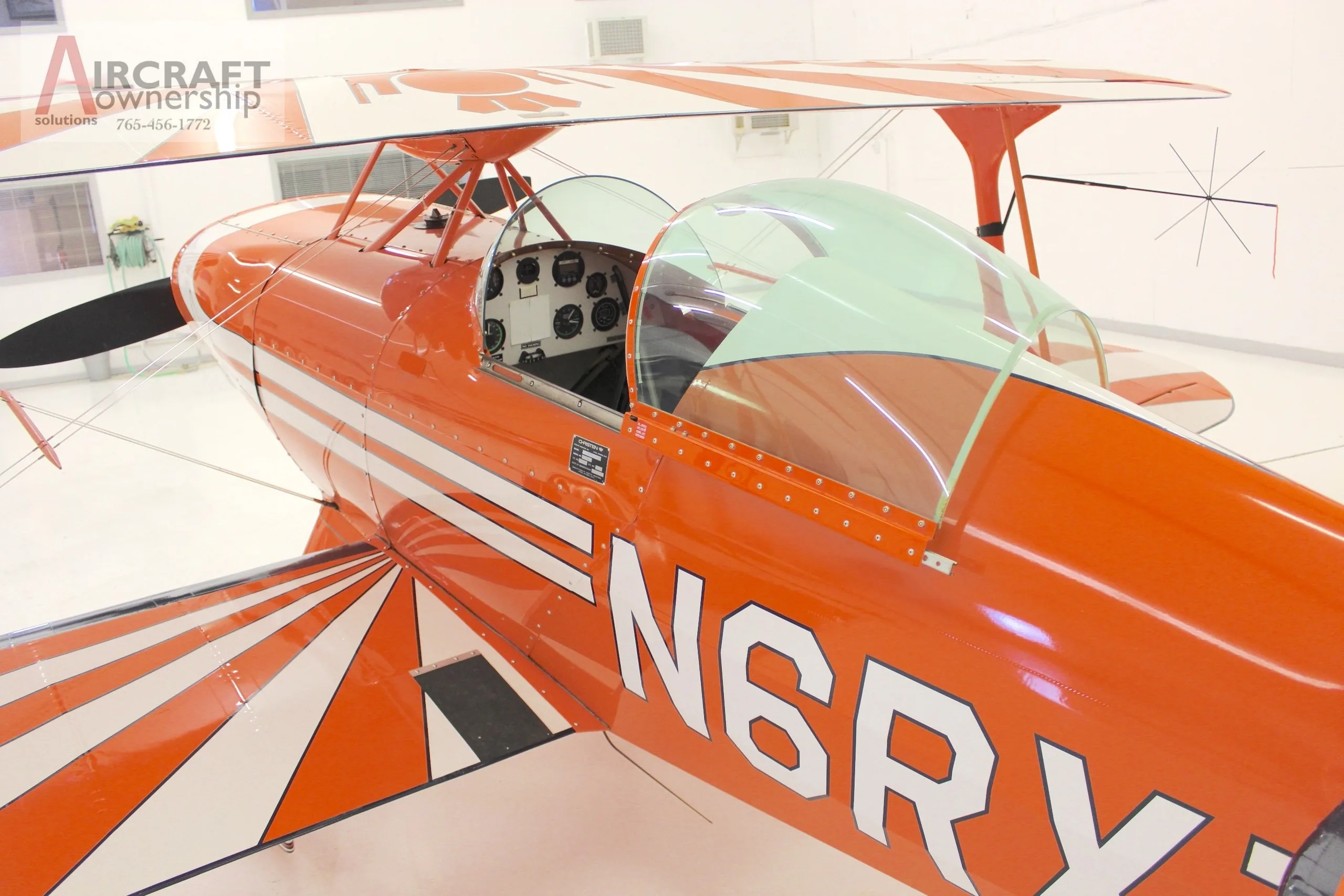 A close-up view of the cockpit and front fuselage of an orange Pitts S-1T biplane, showing the N-number.