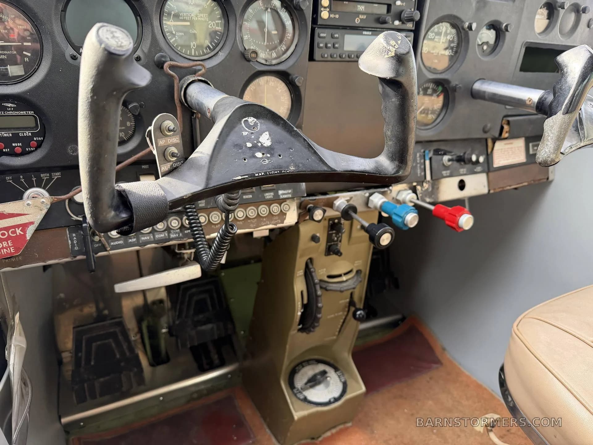 A close-up view of an aircraft cockpit showing the control yoke, rudder pedals, and lower instrument panel.