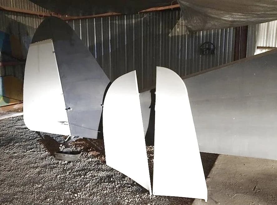 The grey tail section of an aircraft with white control surfaces, seen from the rear in a hangar.