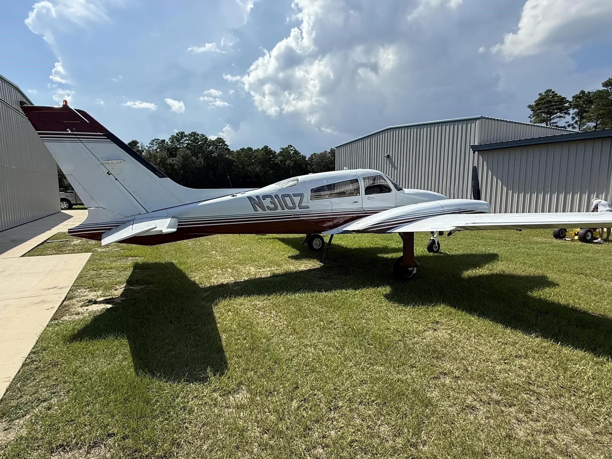 Side-left view of a white and red twin-engine aircraft (N310Z) parked on grass next to a hangar.