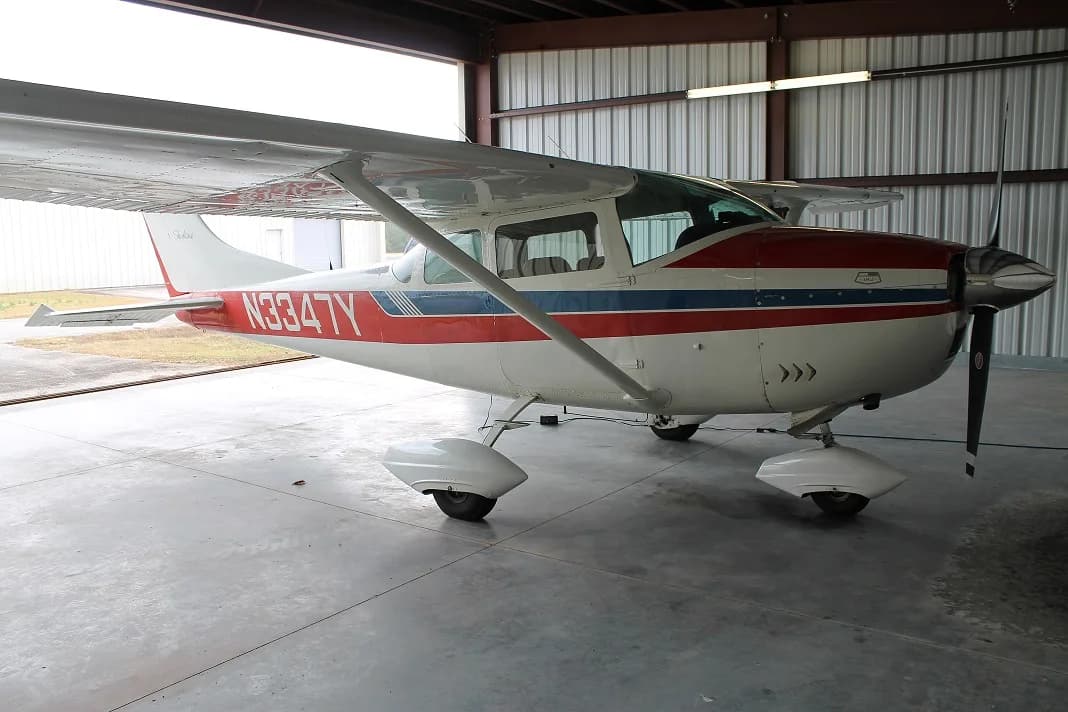 A white and red Cessna 172 Skyhawk aircraft parked inside a hangar.