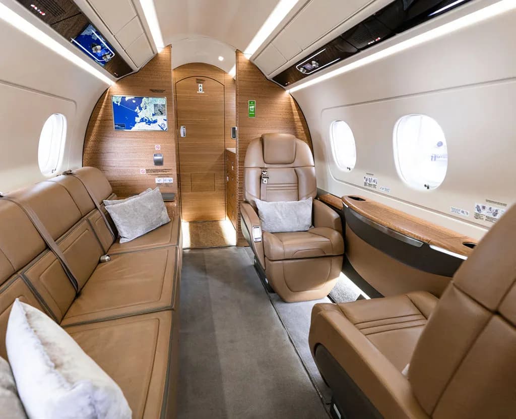 The luxurious interior of a business jet cabin featuring a tan leather sofa and individual seats.