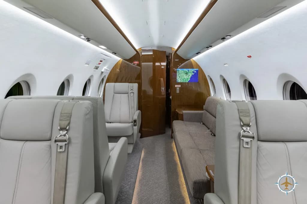 The aircraft cabin interior with light grey leather seats and a long sofa, looking towards the rear.