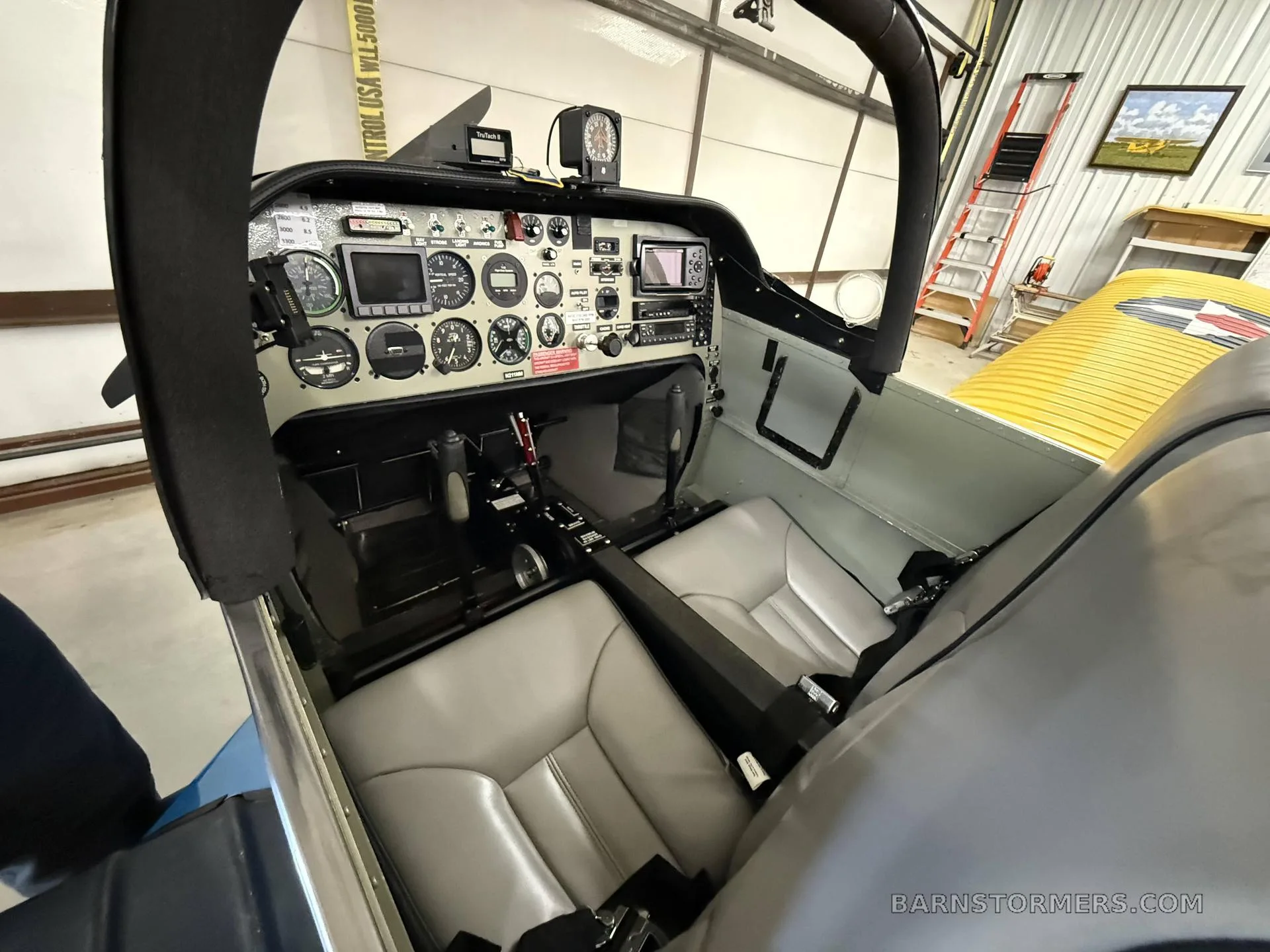View of the aircraft cockpit showing the instrument panel with various gauges and screens, and the two grey seats.