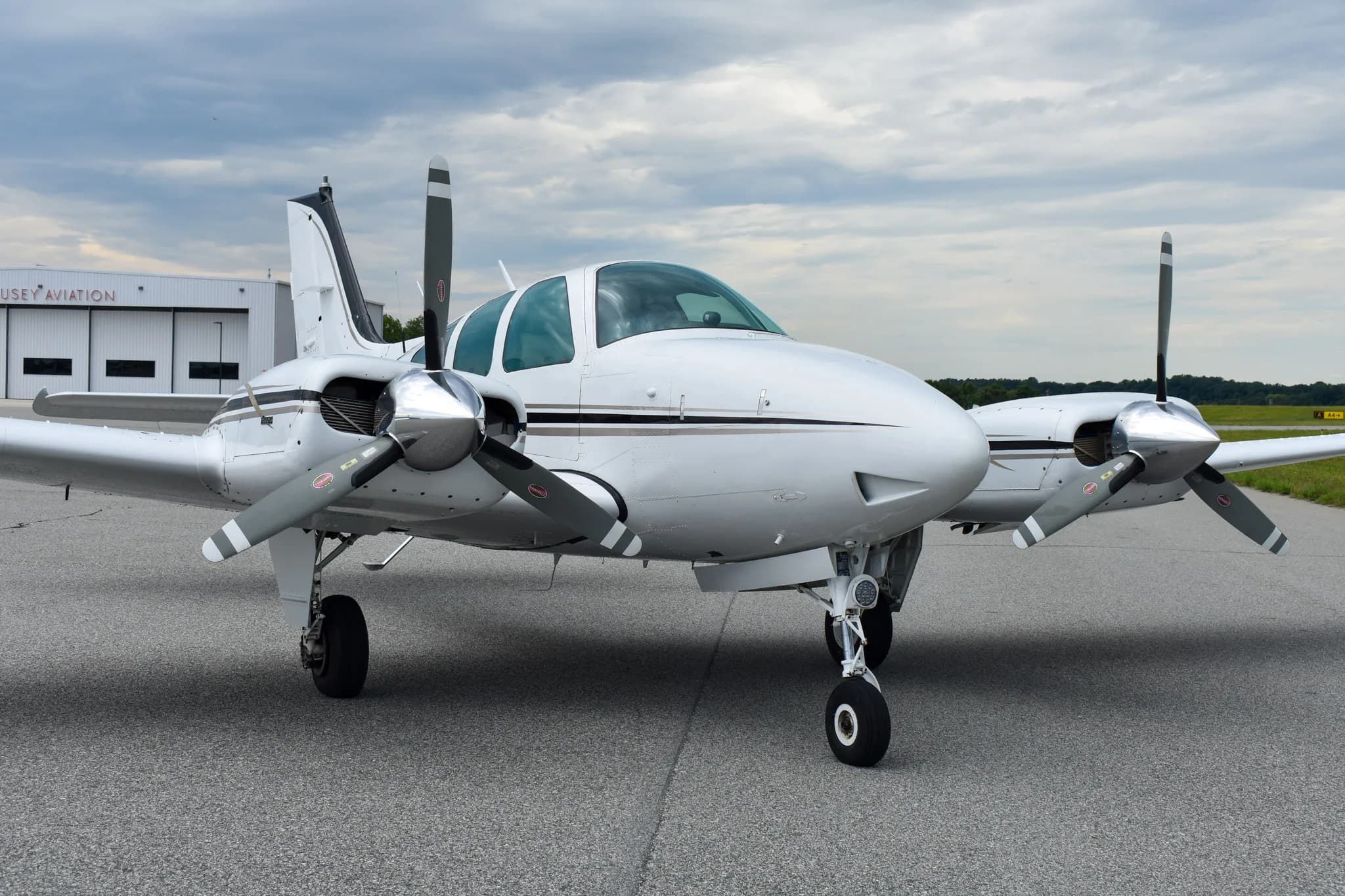 A front view of a white and black Beechcraft Baron aircraft, N6747V, parked on an asphalt runway.